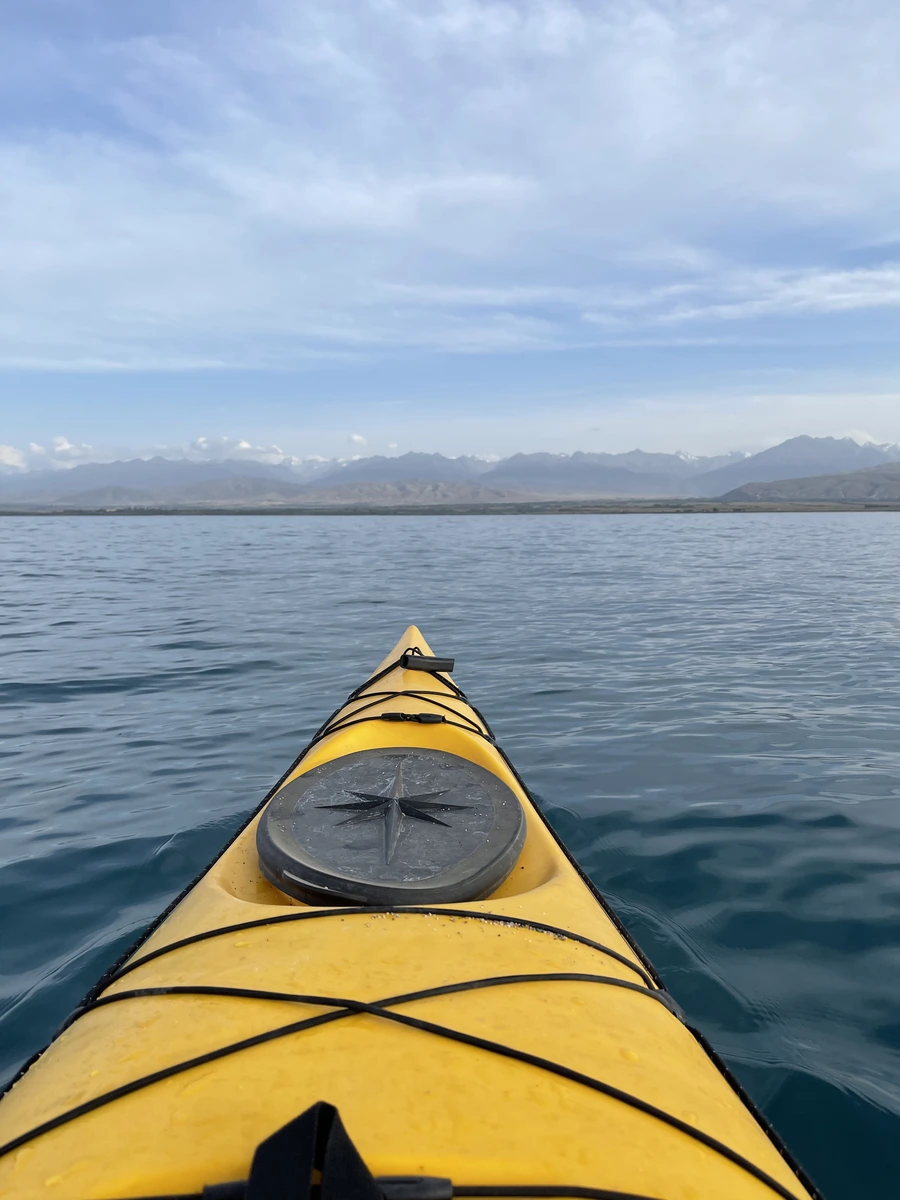 View from a yellow kayak with a compass mounted on the bow, paddling on Issyk-Kul Lake toward distant mountains